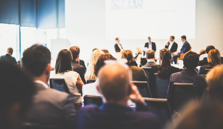 Audience watching a panel discussion at a healthcare conference, where health plans gather to discuss NEMT access
